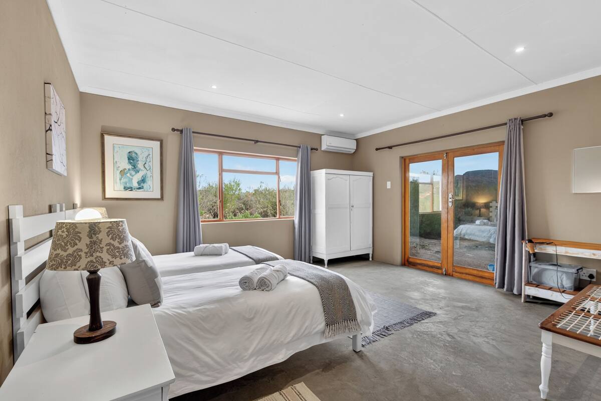A bedroom with two beds, a desk, a wardrobe, and a view of the outdoors.