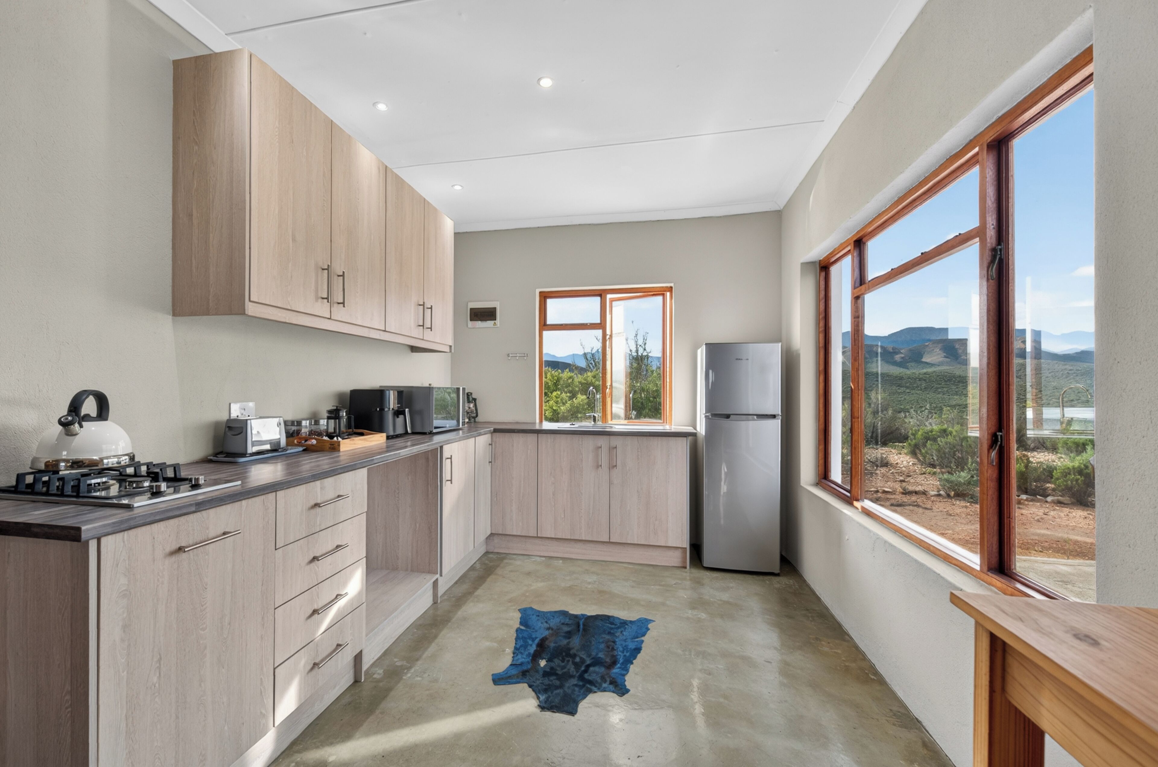 A modern kitchen with wooden cabinets, a gas stove, a refrigerator, and a window with a view of the landscape.