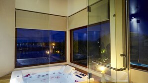 Un baño moderno con una bañera de hidromasaje de vidrio, suelo de madera y ventanas amplias que dan al exterior.