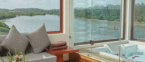 A modern bathroom with a glass-enclosed shower, a wooden bench, and a view of a lake.