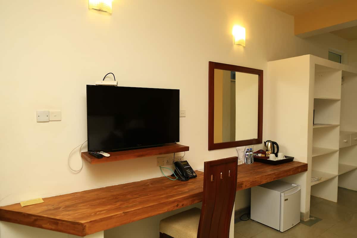 Ein Hotelzimmer mit Schreibtisch aus Holz, einem Fernseher, einem Spiegel, einem Minikühlschrank und einer Kaffeemaschine.