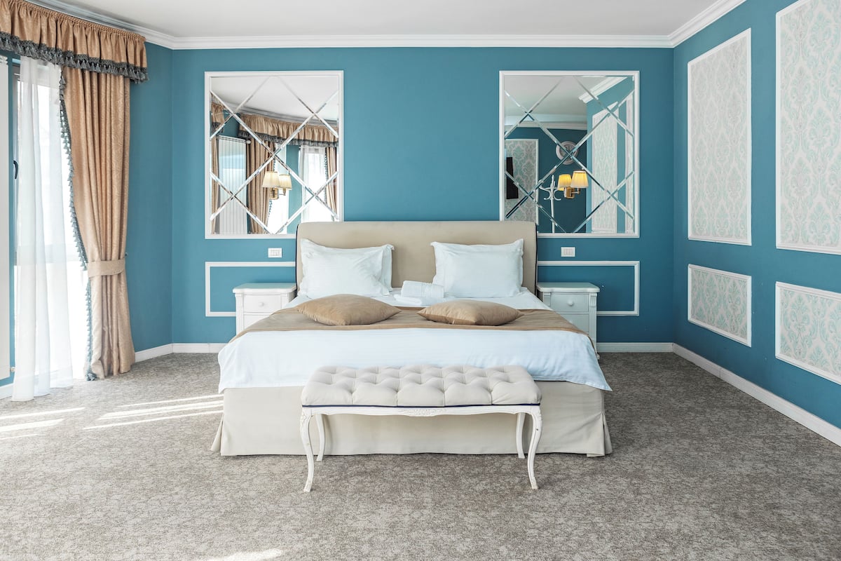 A bedroom with a large bed, two nightstands, a bench, and a mirror.