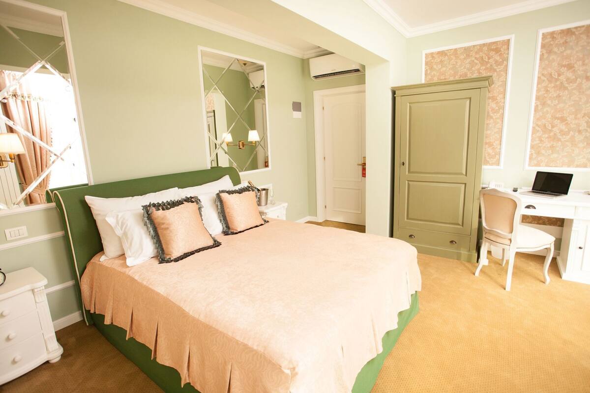 A bedroom with a bed, a desk, a chair, a wardrobe, and an air conditioning unit.