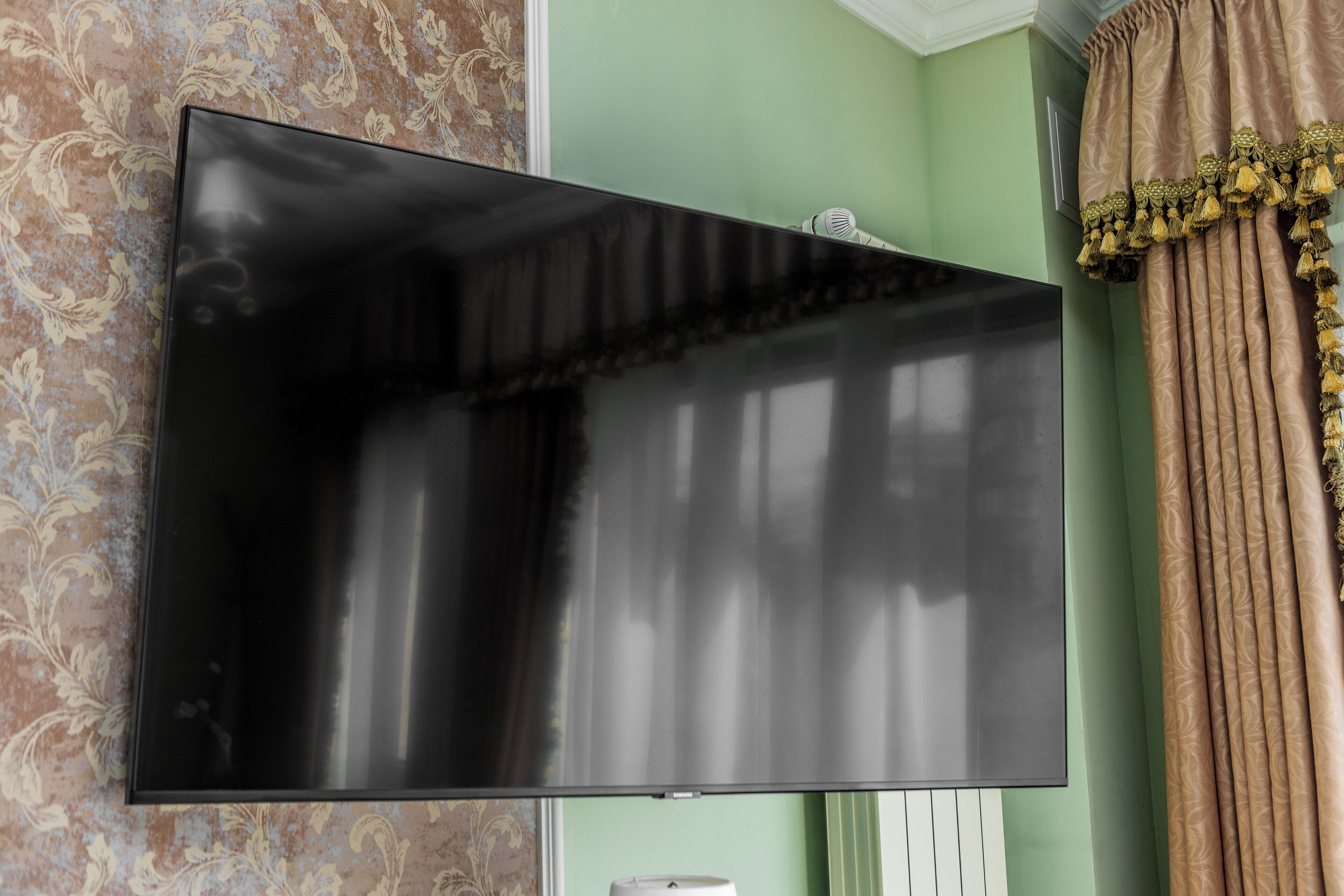 Un televisor de pantalla plana montado en una pared con papel tapiz estampado y una cortina.