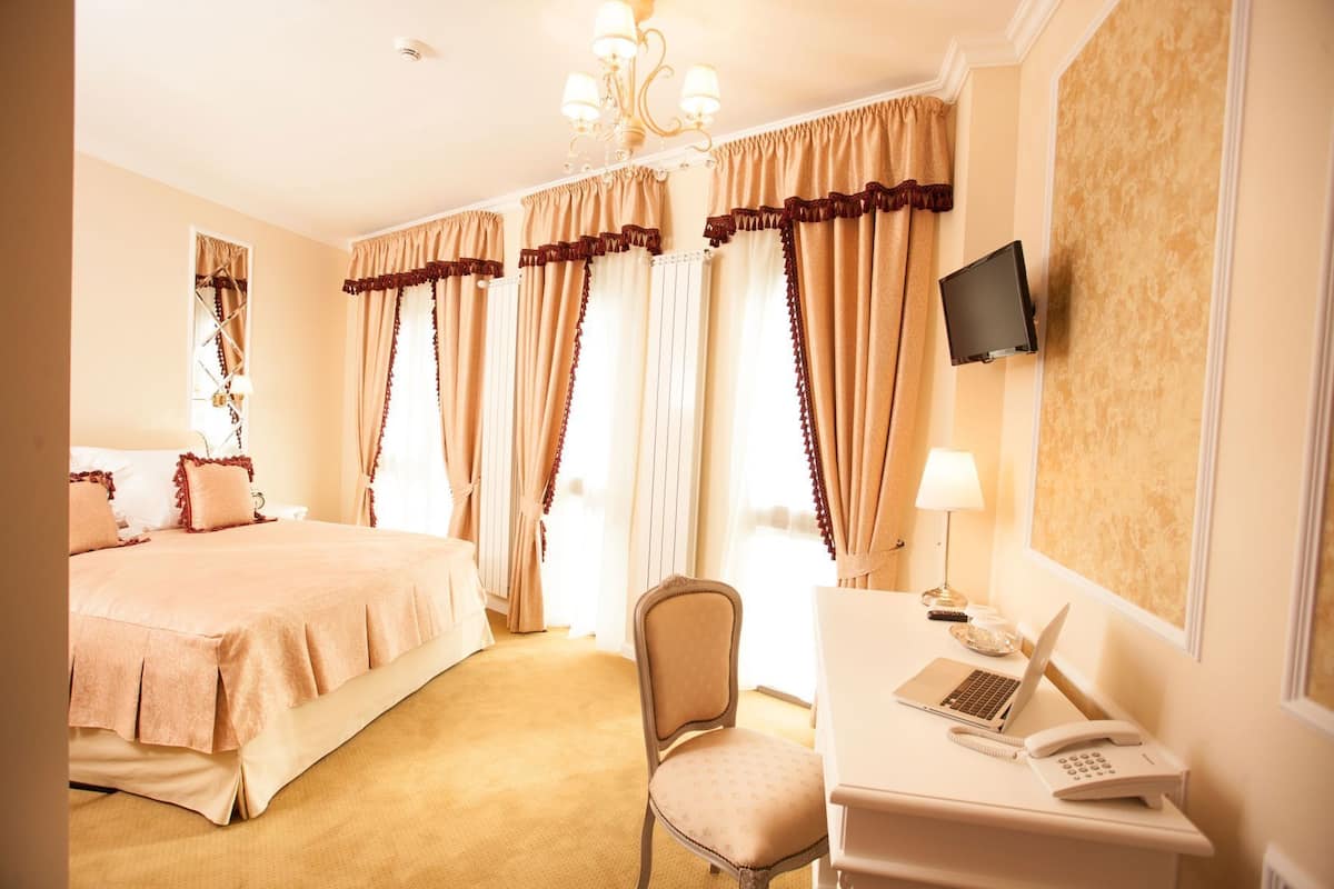 A hotel room with a bed, a desk with a laptop and phone, a chair, and a TV on the wall.