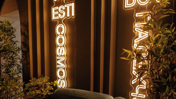 Un área de lounge moderna con un letrero de neón que dice "TU COSMOS" y "BOY BOY" en una tipografía elegante.