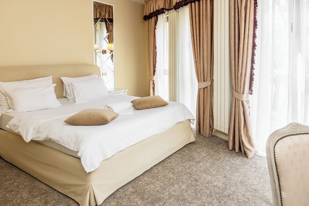 A neatly made bed with white and beige bedding, a nightstand, and a chair.