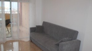 Um quarto com um sofá cinzento, uma porta de vidro e um chão de azulejos.