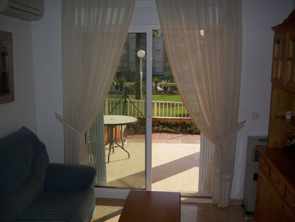 A living room with a sofa, a table, and a sliding glass door leading to a balcony with a table and chairs.