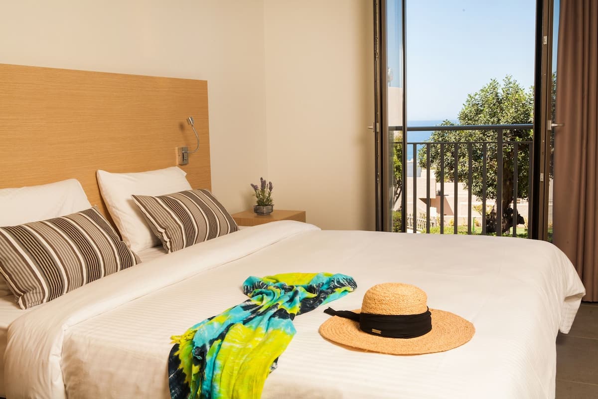 A hotel room with a large bed, a balcony with a view, and a small table with a plant.
