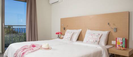 A hotel room with a large bed, a nightstand with a book and a plate, a window with curtains, and an air conditioning unit.