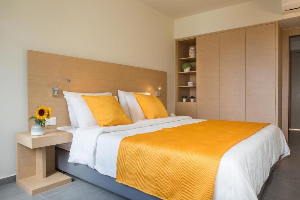 A modern bedroom with a wooden headboard, a bed with white and yellow bedding, a bedside table with a vase of sunflowers, and built-in shelving with decorative items.