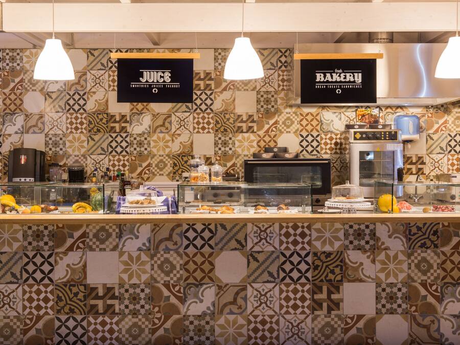 A bakery and juice bar counter with a patterned tile backsplash and hanging pendant lights.