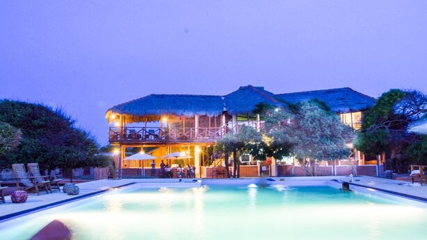 A large resort with a swimming pool, outdoor seating, and a thatched-roof building.