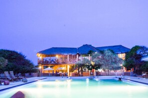 Un gran resort con piscina, mobiliario exterior y un edificio con techo de paja.