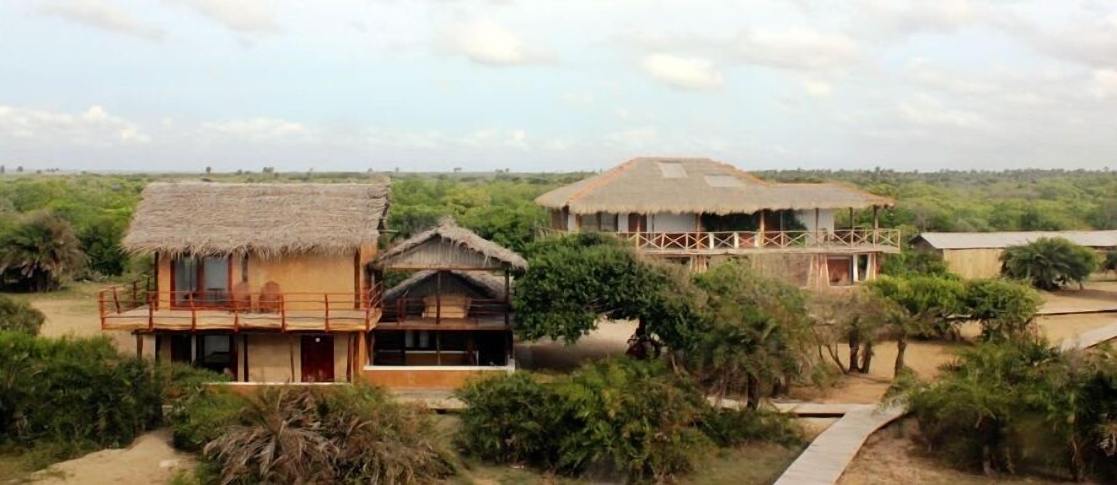A bungalow with a thatched roof, surrounded by greenery and a clear sky.