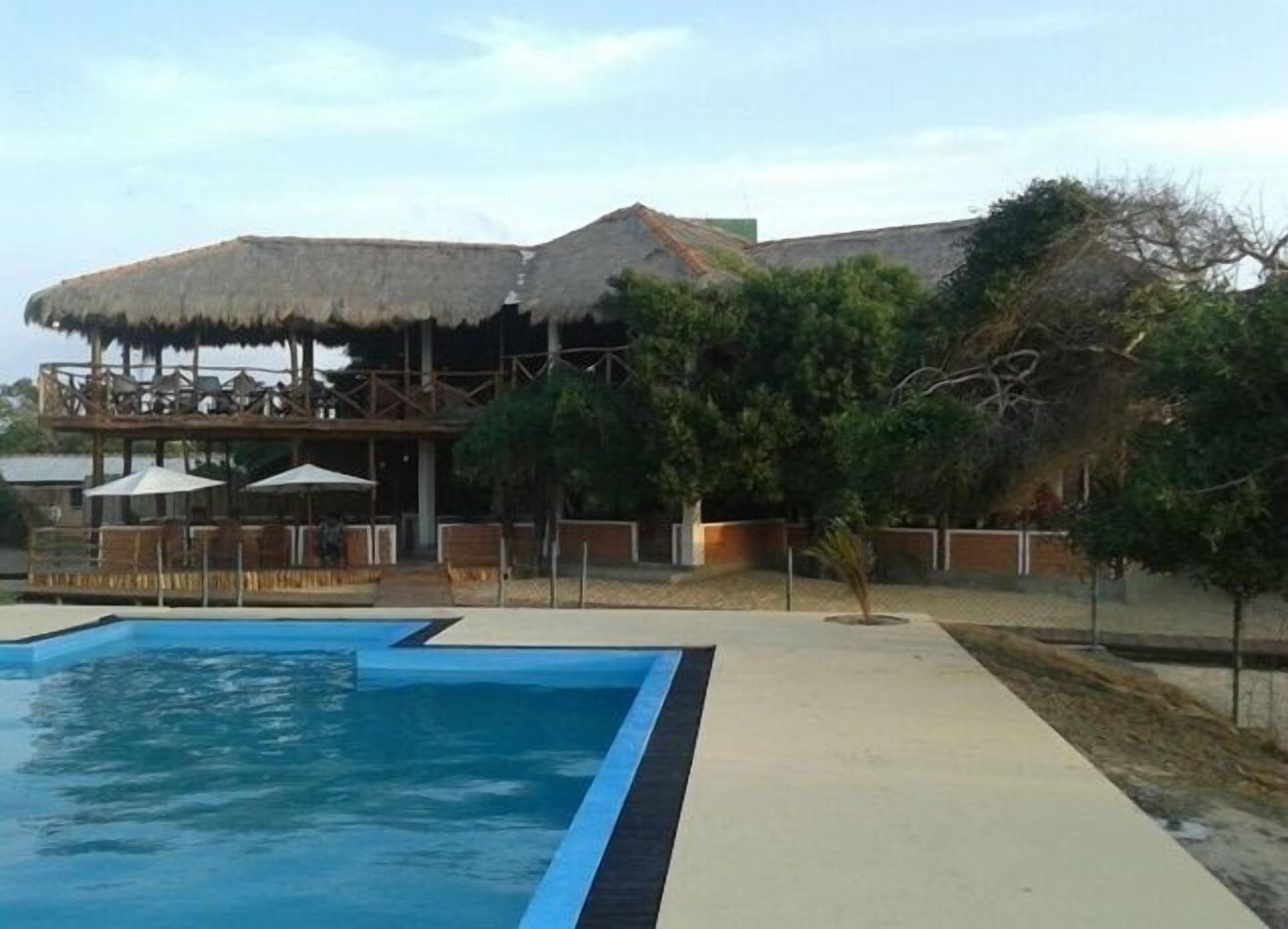 A swimming pool with a thatched-roof structure and lounge chairs in the background.