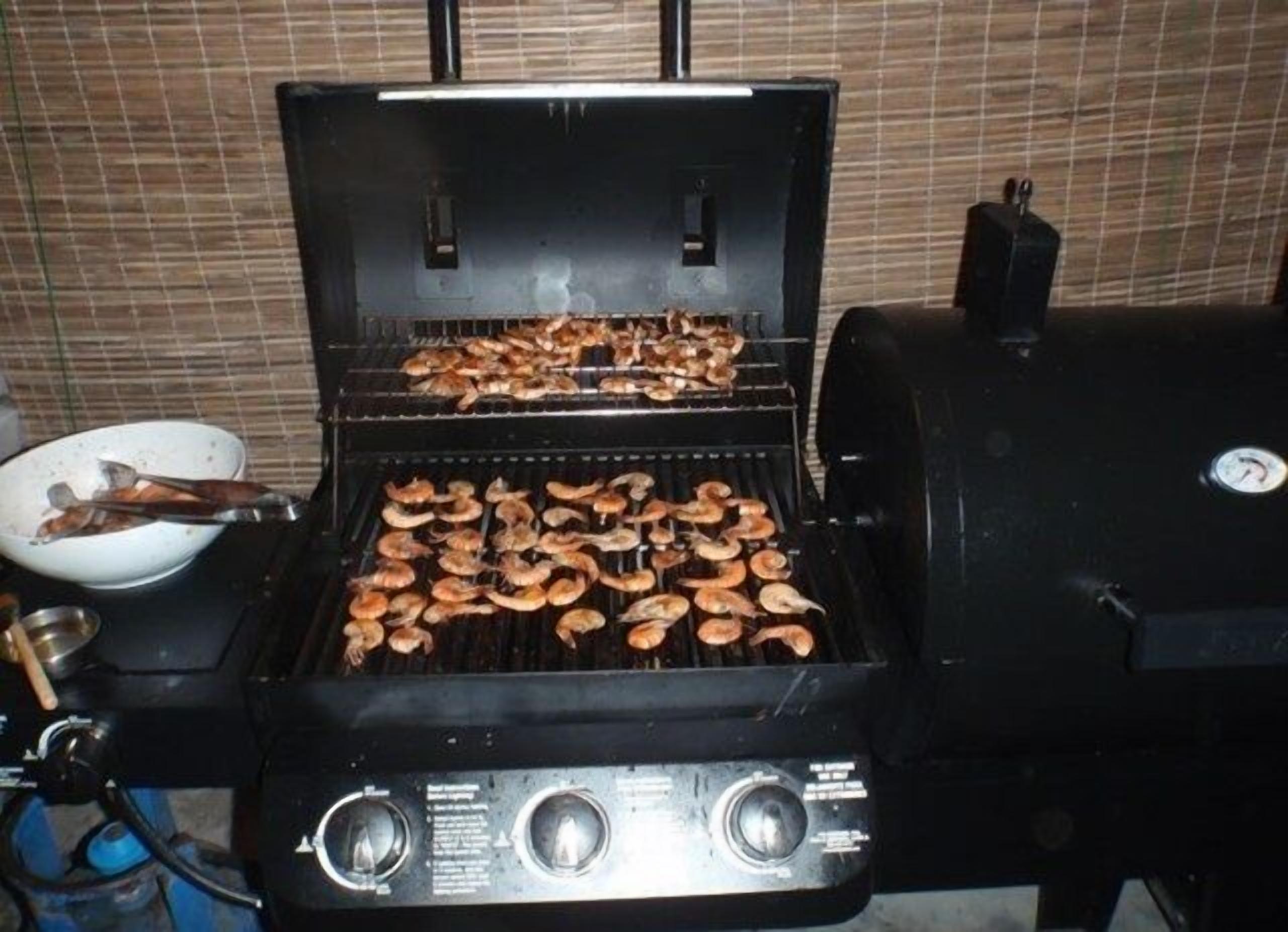 A grill with multiple cooking grates, a control panel with knobs, and a pair of tongs on the left side.