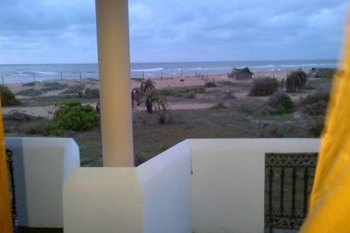 Vista da praia com paisagem arenosa, vegetação e céu nublado.