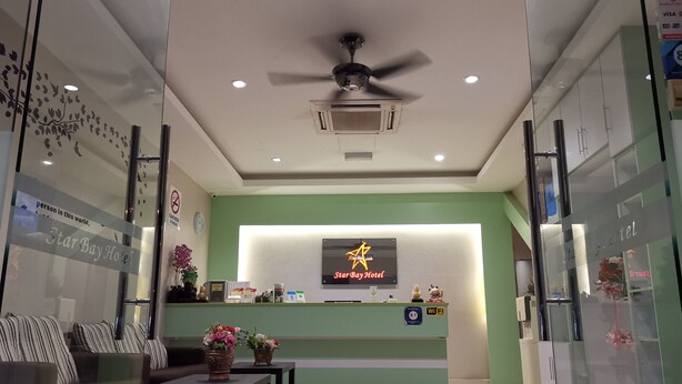 A hotel reception area with a green wall, a reception desk, a ceiling fan, and a clock on the wall. - Star Bay Hotel (Lumut)