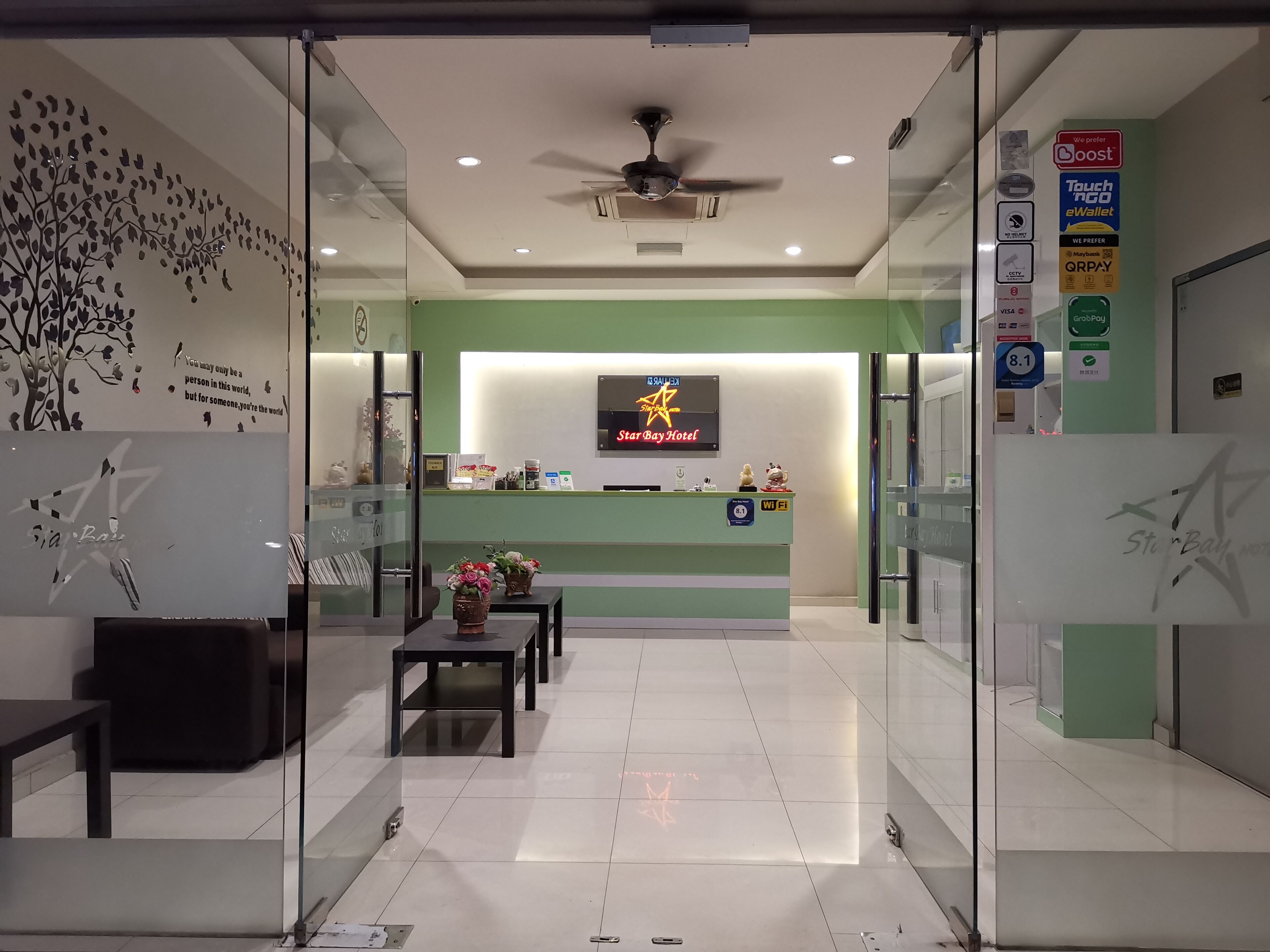 A hotel reception area with a Star Bay Hotel sign, a reception desk, a ceiling fan, and a glass wall with a decorative tree design.