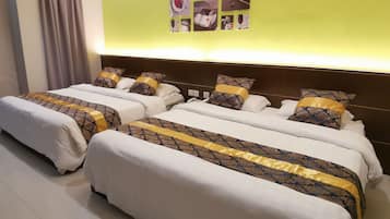 A hotel room with two beds, each with patterned bedding and pillows, a wall with a photo collage, and a curtain on the left.