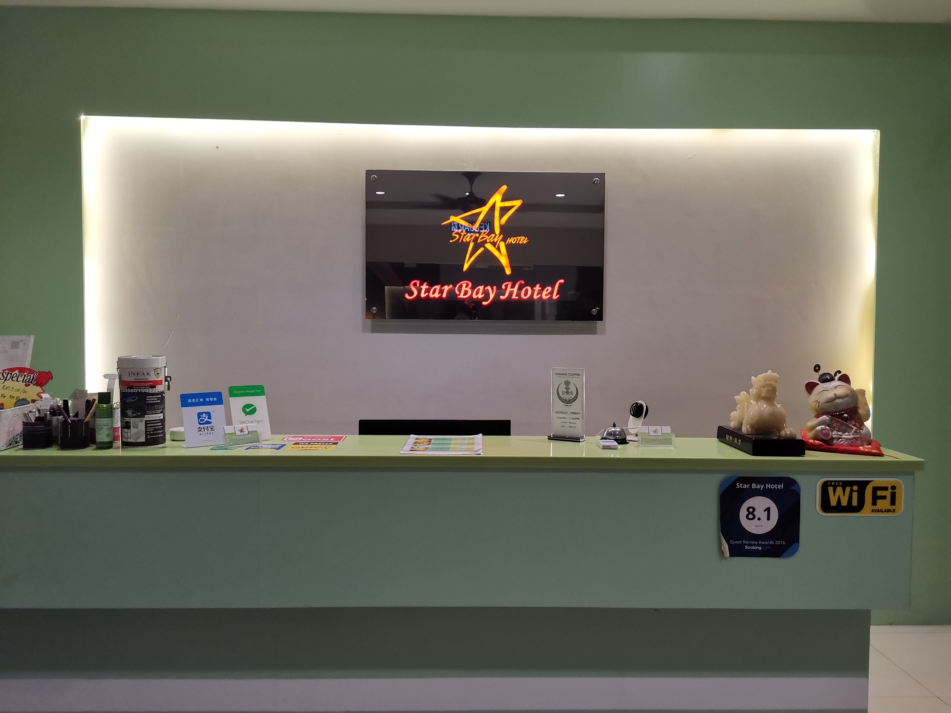 Un comptoir d’accueil d’hôtel avec une enseigne « Star Bay Hotel », un symbole Wi-Fi et une plaque commémorative récompensant les commentaires positifs des clients.