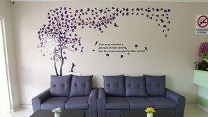 A modern living room with a dark blue sofa set, two matching dark wooden coffee tables, and a decorative wall mural featuring a tree and birds. - Star Bay Hotel (Lumut)