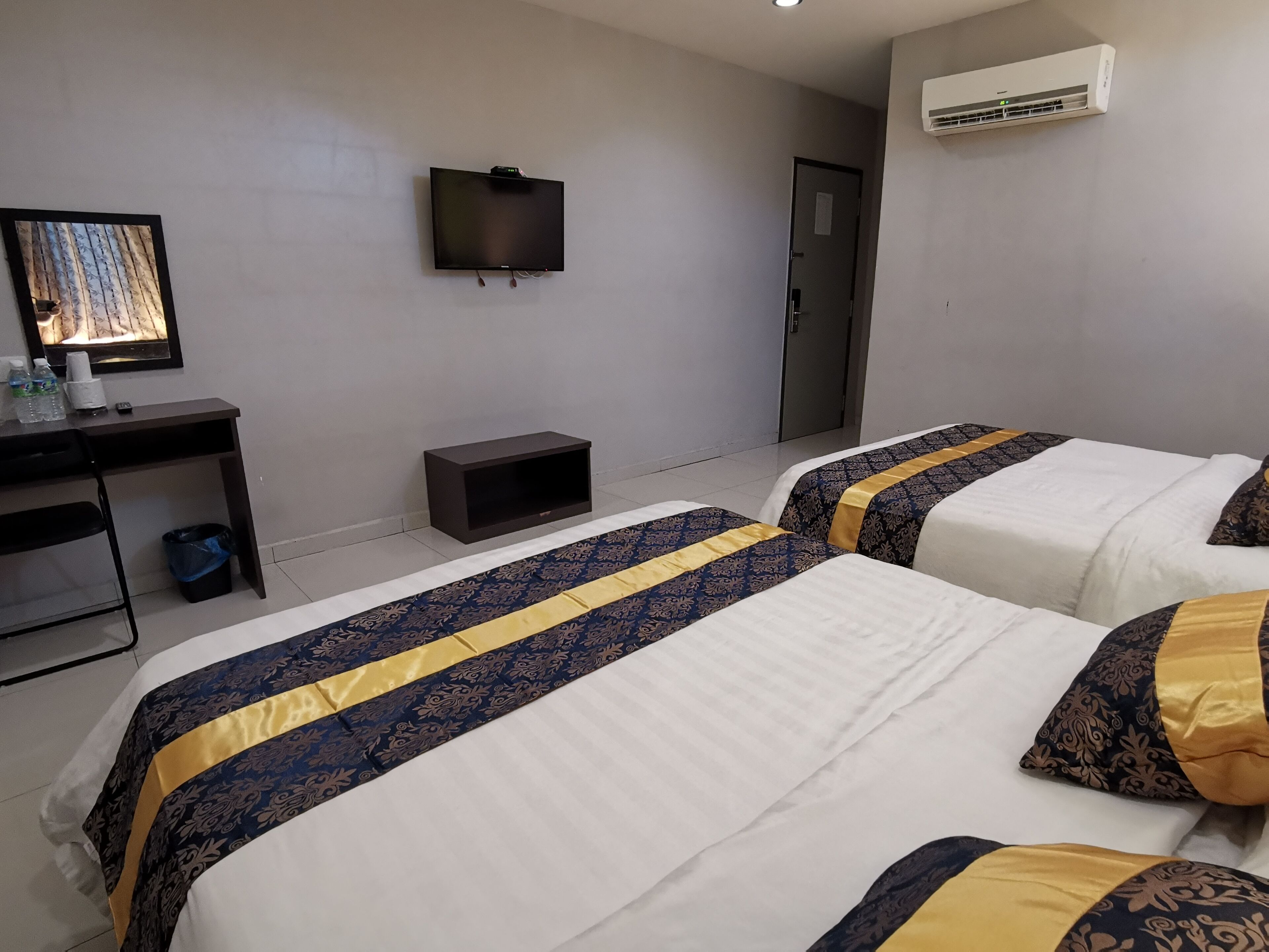 A hotel room with two beds, a desk, a chair, a TV, and an air conditioning unit.