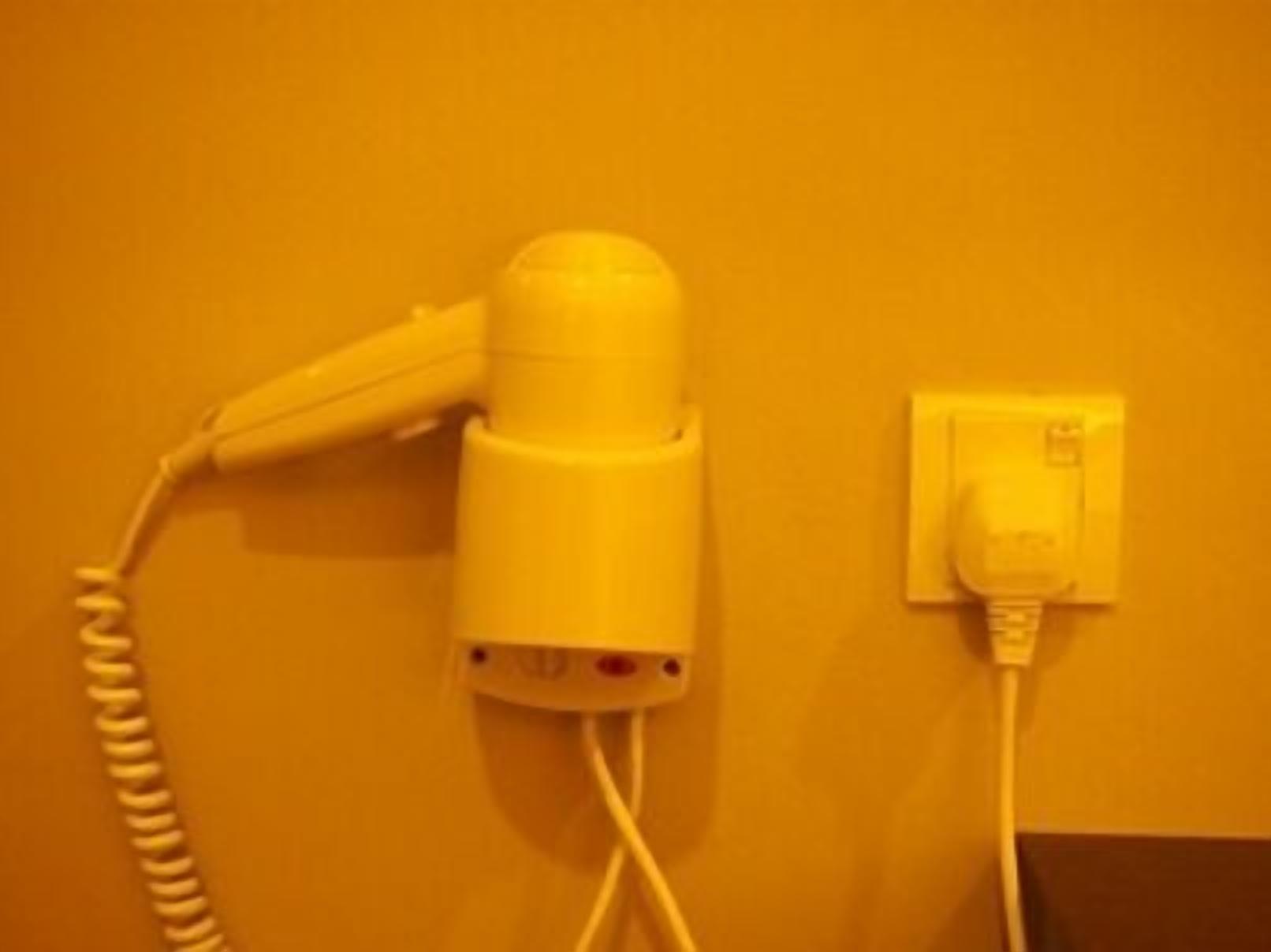 A hairdryer and a power outlet on a yellow wall.