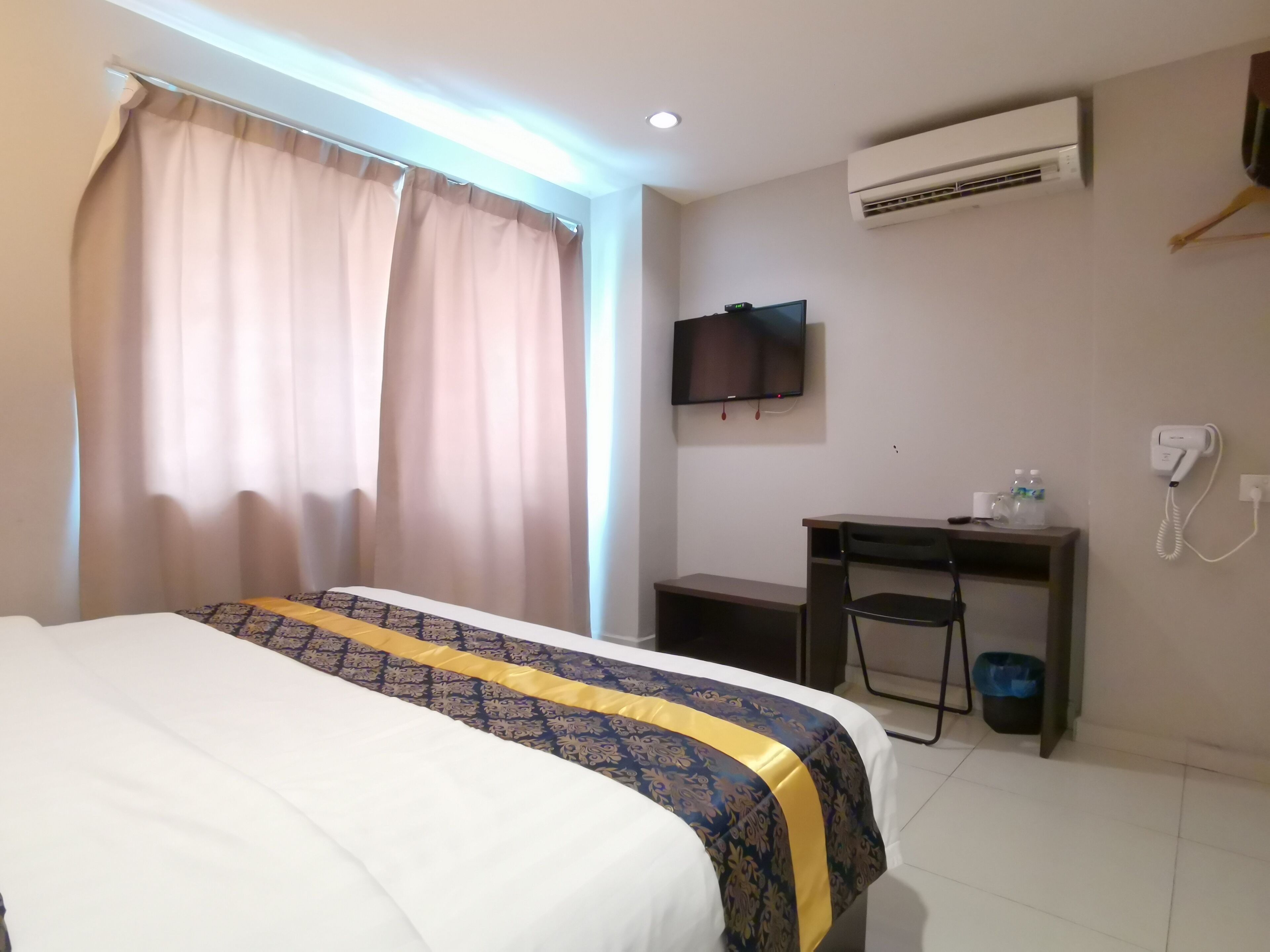 Hotelkamer met een bed, een bureau, een stoel, een televisie, een airconditioner en een telefoon.