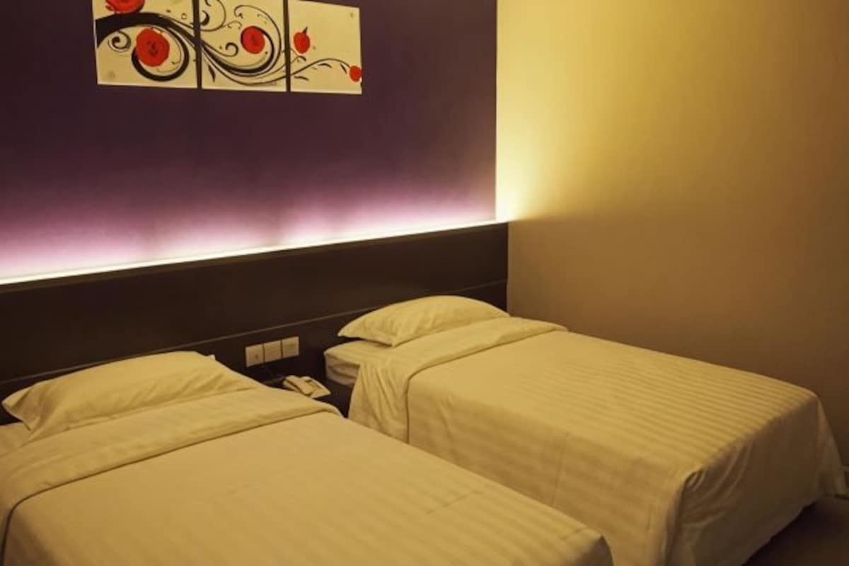 Habitación de hotel con dos camas, una mesita de noche y una obra de arte colgada en la pared.