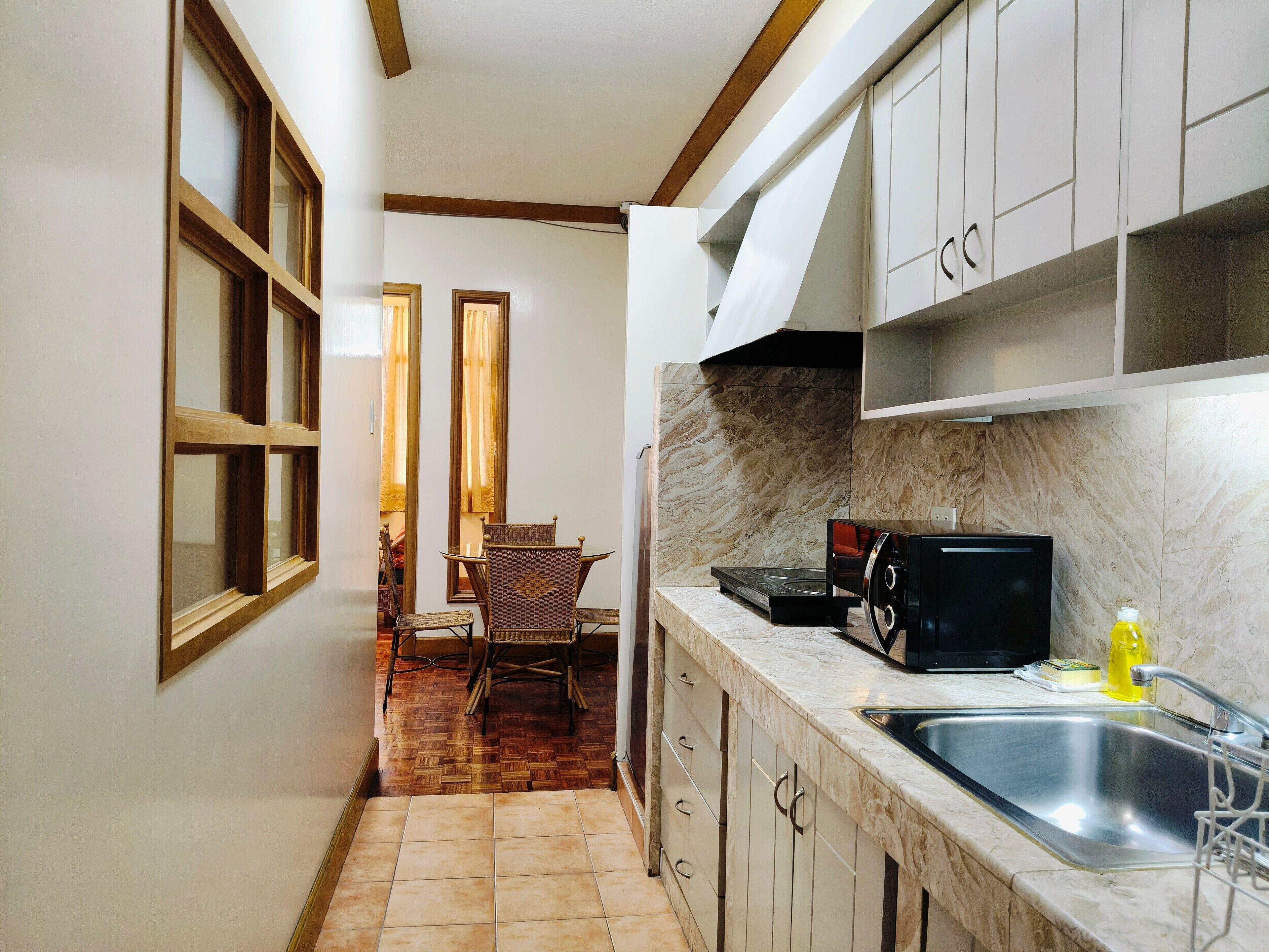 A narrow kitchen with a tiled floor, wooden cabinets, a stainless steel sink, and a microwave.