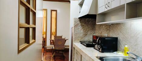 A narrow kitchen with a tiled floor, wooden cabinets, a stainless steel sink, and a microwave.