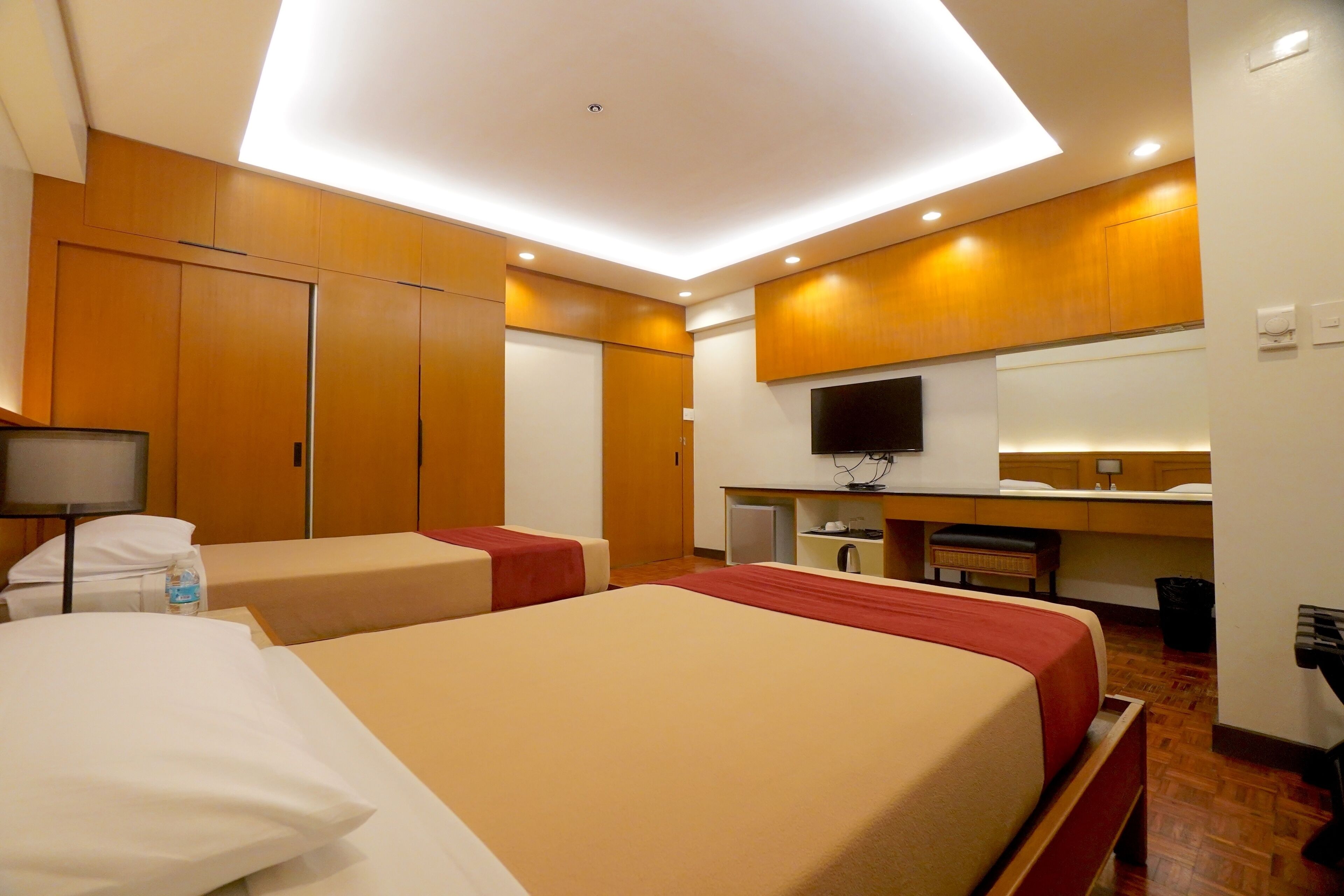 Ein Hotelzimmer mit zwei Betten, einem Fernseher, einem Schreibtisch und einem Kleiderschrank.