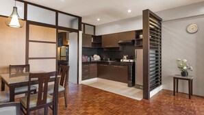 A modern kitchen with wooden cabinets, a dining area with a table and chairs, and a small side table with a vase. - Tropicana Suites (Manila)