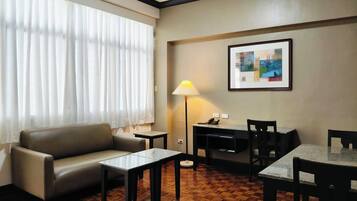 A hotel room with a sofa, a small table, a desk with a lamp, and a framed picture on the wall.