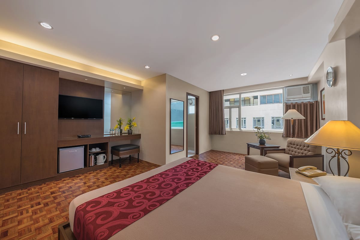 A hotel room with a bed, a desk, a television, a minibar, and a window with curtains.