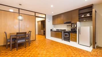 A modern kitchen with wooden flooring, built-in cabinets, a refrigerator, and a dining area with a table and chairs.