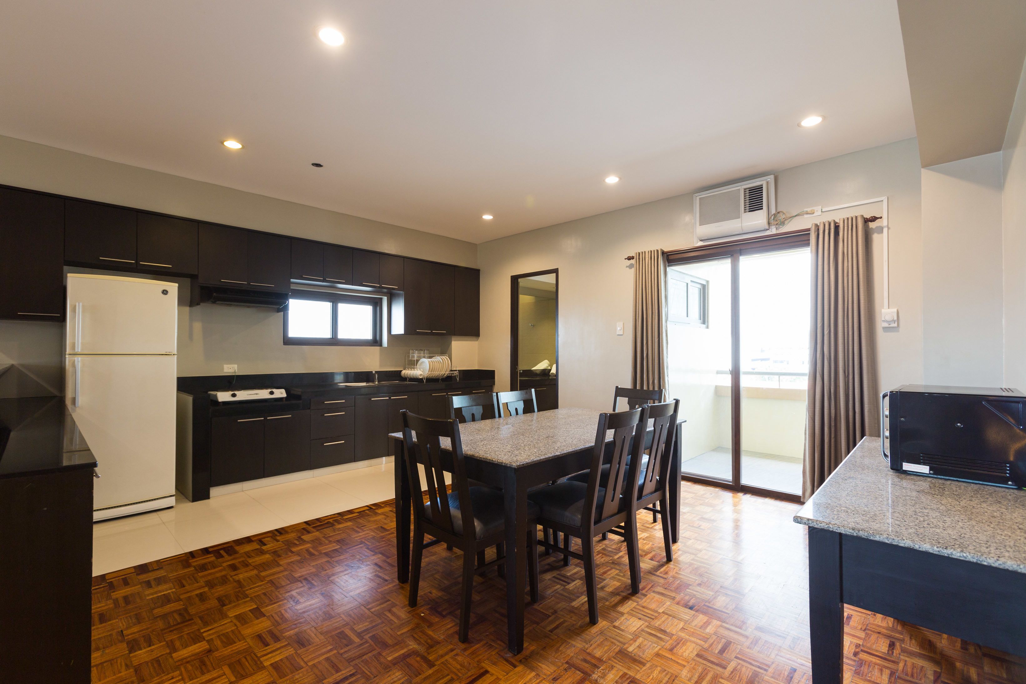 A modern kitchen with dark cabinets, a white refrigerator, and a dining area with a table and chairs.