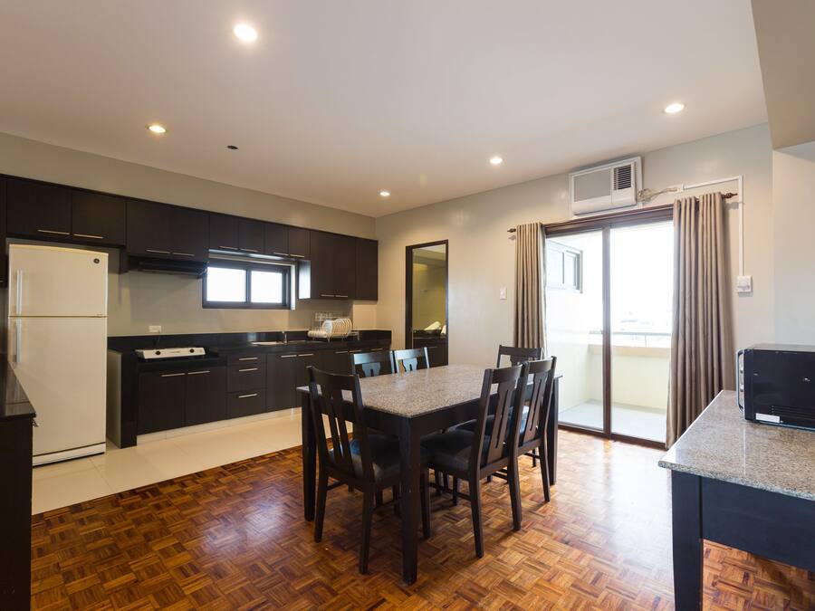 Una cocina moderna con armarios oscuros, un refrigerador blanco y un comedor con una mesa y sillas.