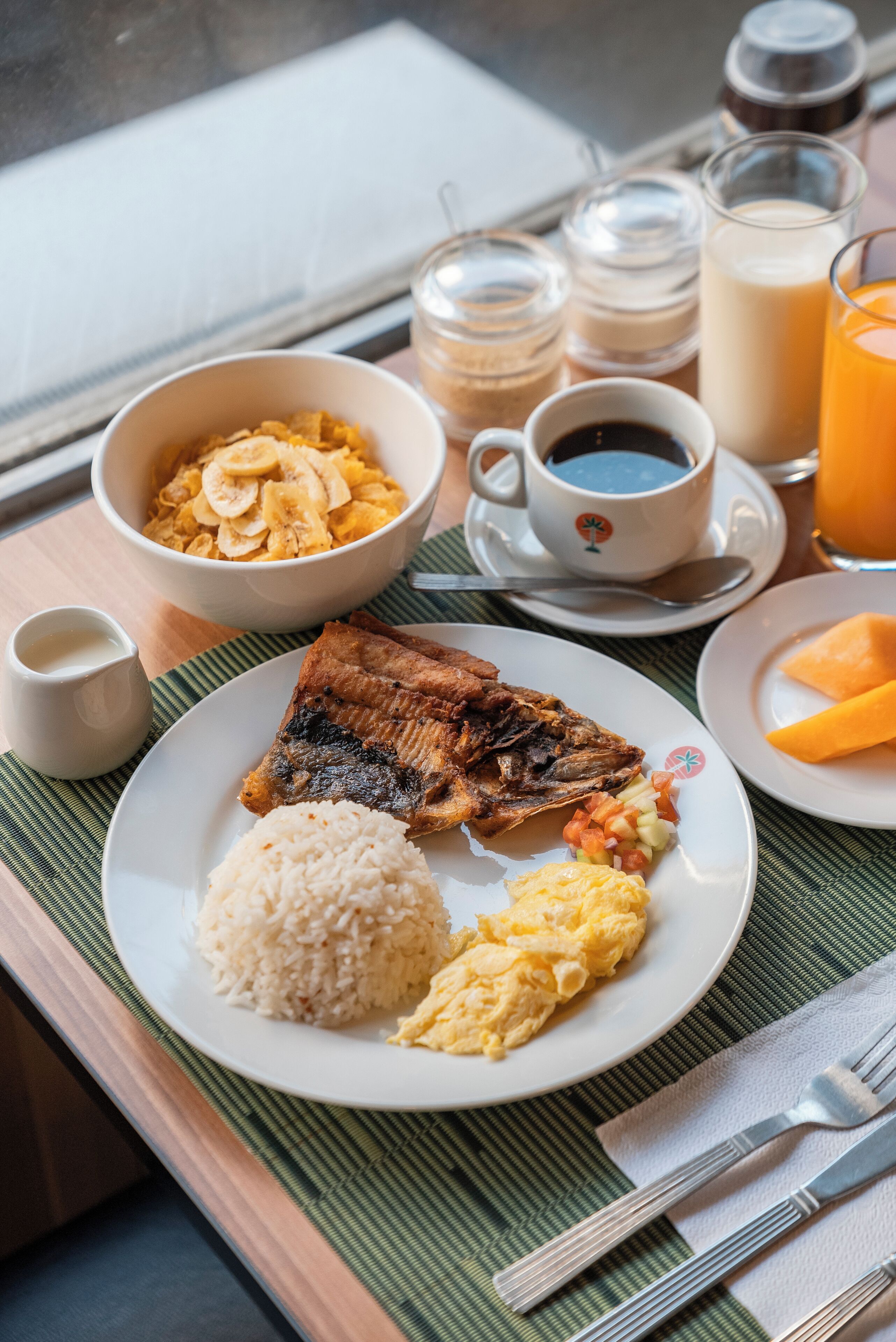 Un plateau repas comprenant du riz, des œufs brouillés, du poisson frit et un bol de fruits.