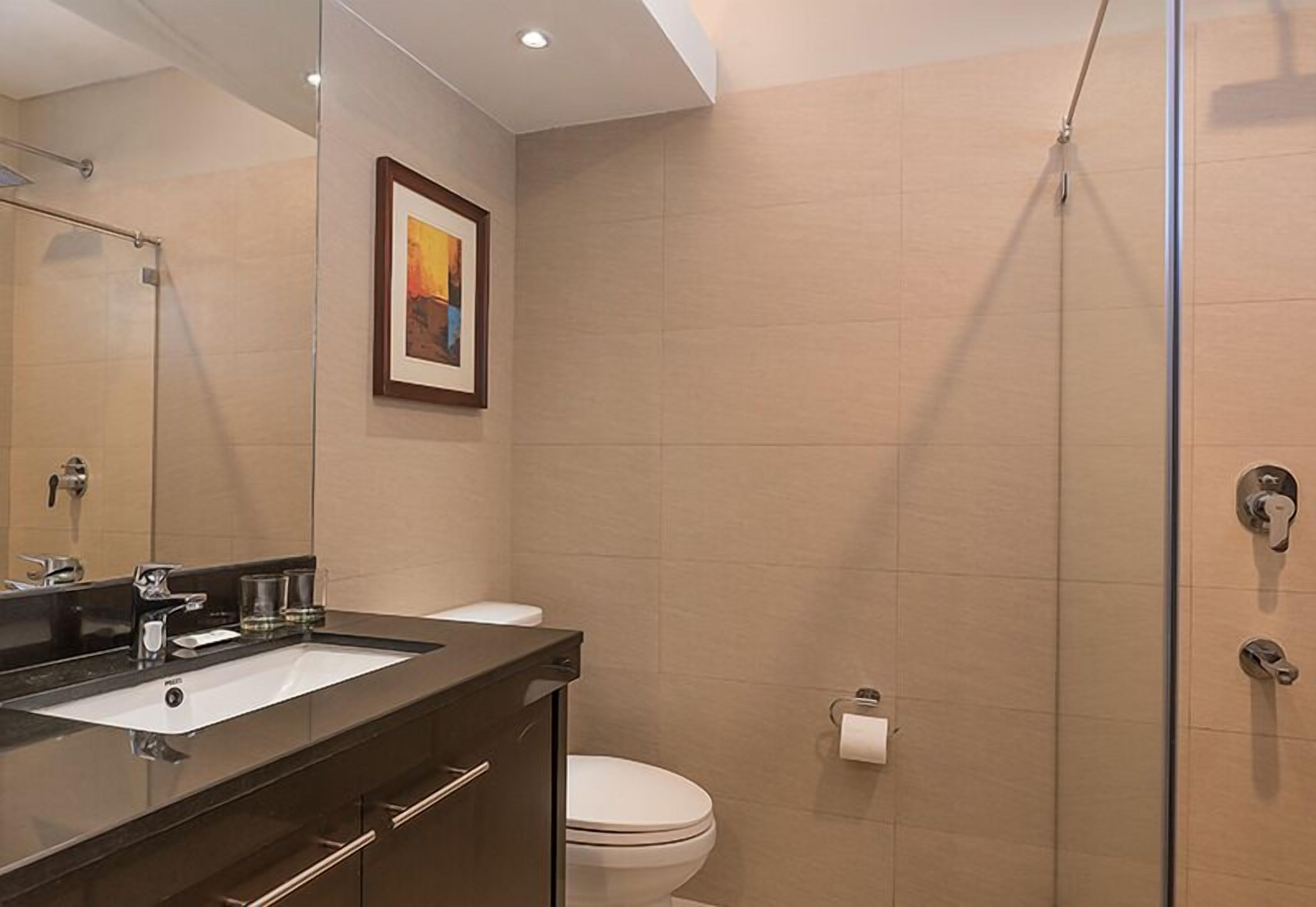 A modern bathroom with a glass shower enclosure, a white toilet, and a black vanity with a mirror.