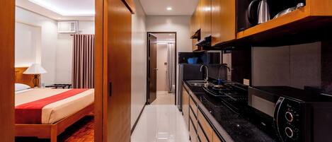 Habitación de hotel con cama, un escritorio pequeño, una kitchenette con estufa y microondas, y un baño con cortina de ducha.