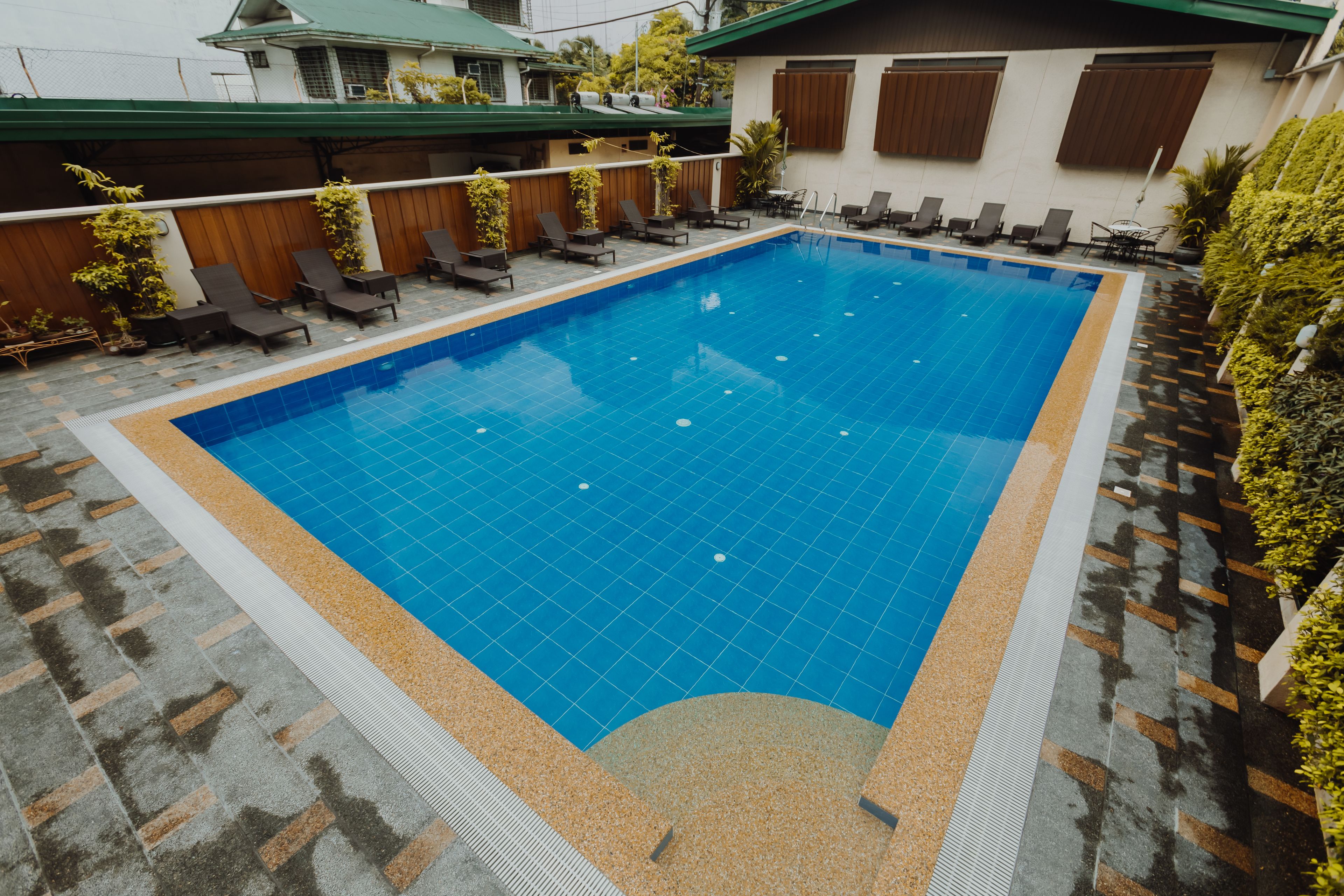 Une piscine rectangulaire dont le bord est recouvert de carreaux, entourée de chaises longues et de plantes en pot.