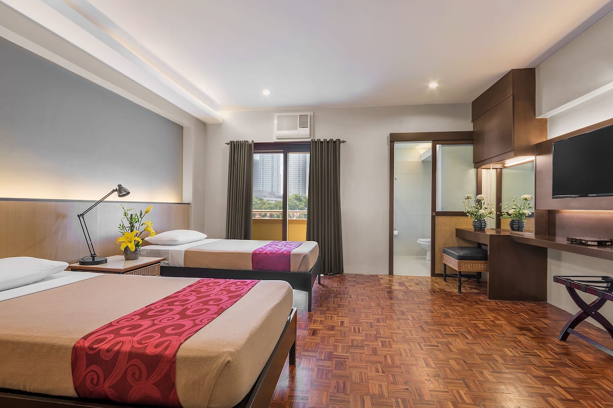 A hotel room with two beds, a desk, a TV, and a balcony with curtains.