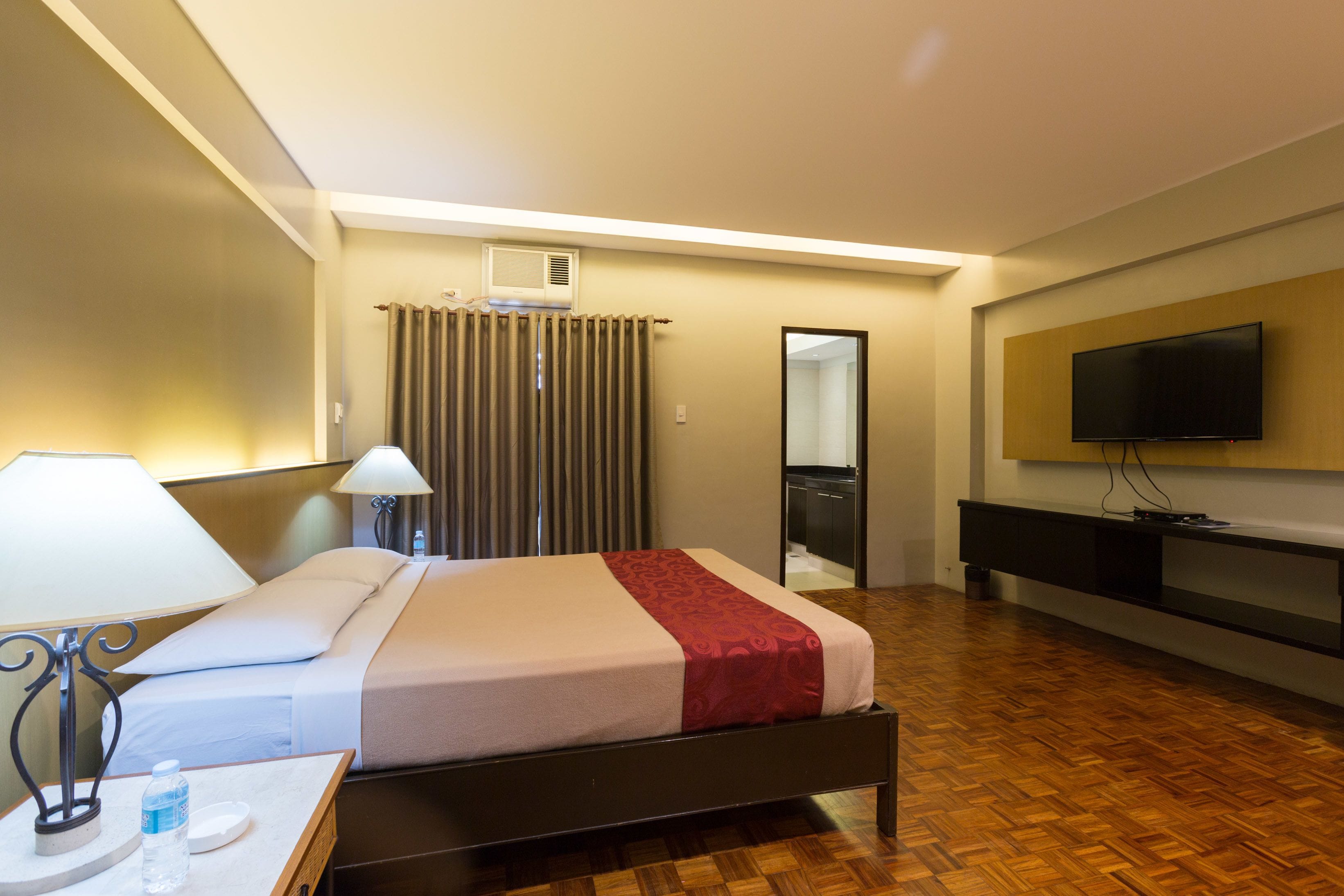 Una habitación de hotel con cama, mesita de noche, lámpara y televisión montada en la pared.