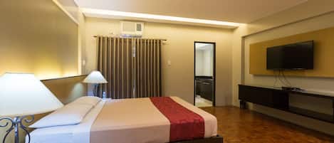 Una habitación de hotel con cama, mesita de noche, lámpara y televisión montada en la pared.