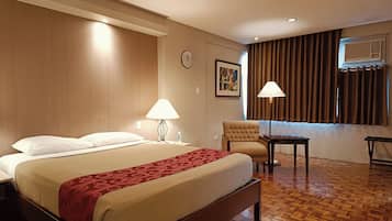 Habitación de hotel con una cama grande, un escritorio, una silla, una lámpara, un reloj y una ventana con cortinas.
