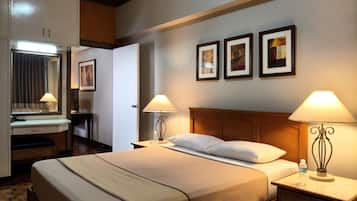 A hotel room with a large bed, bedside tables with lamps, a dresser, a mirror, and framed pictures on the wall.